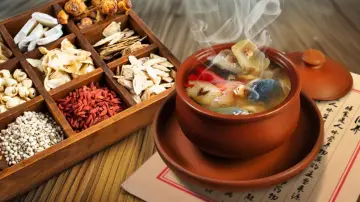 Wooden box of dried soup ingredients beside a steaming Cantonese clay pot soup